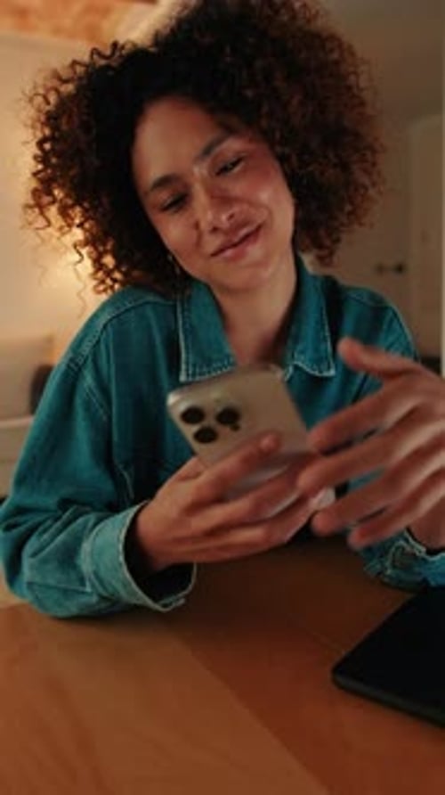 Smiling woman sitting at table in living room having fun with mobile phone