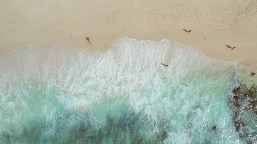 Ruhiger Strand mit Wellen, die sanft den Sand berühren, und ein paar Menschen, die die Küste entlang laufen