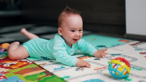 Active baby in blue clothes lies on a colorful mat. Funny kid is happy about a toy in front of him.