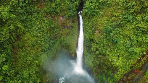 Aerial view of a tall rainforest waterfall plunging into a pool in Costa Rica