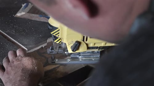 A Carpenter in His Workshop Saws with an Electric Jigsaw Makes Wooden Parts