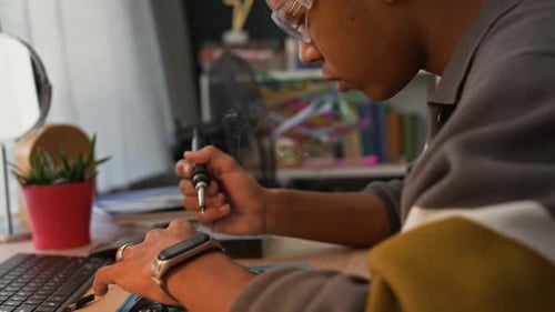 Young Adult Solder Repairing Circuit Board at Desk