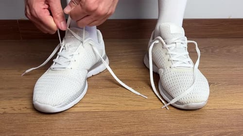 Close Up of a Woman Tying Shoelaces on White Sneakers Indoors Sport Shoes on Wooden Floor Preparing