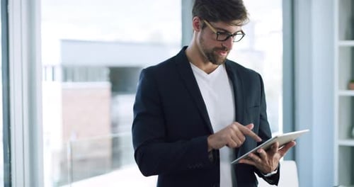 4k video footage of a handsome young businessman using a digital tablet in his office