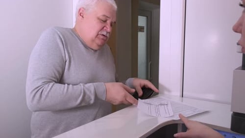 Elderly Man Client Signing Paper at Reception Desk In Medical Clinic