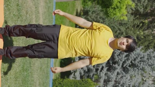 Vertical Video of Young man exercising in the park doing body stretches with his arms.