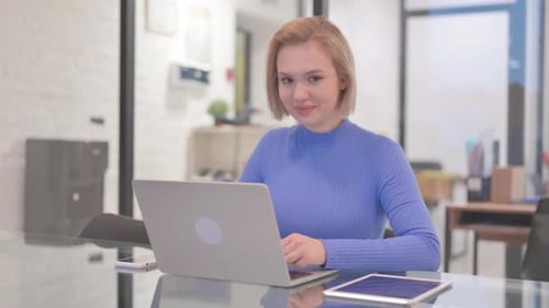 Young Woman with Thumbs Up while Working on Laptop in Office