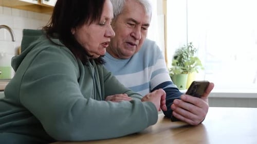 Senior Couple Using Smartphone Together Indoors