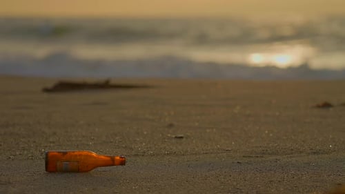 Eine einzige Flasche bleibt übrig, um das Meer mit dem Sonnenuntergang im Hintergrund zu verschmutzen
