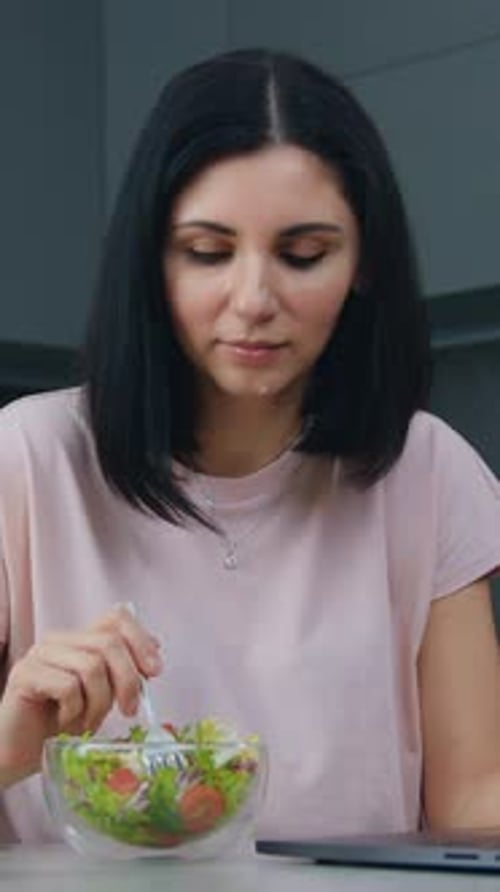 Woman Eats Salad While Working on Laptop