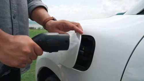 Progressive Man Connect Power Cable to His Ecofriendly EV Car on Green Field