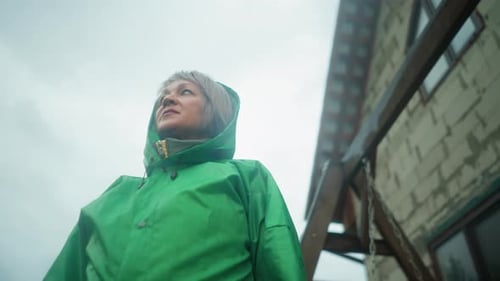 Woman in Green Raincoat Looking Focused Under Bright Sky Near Swing Bench