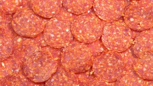 Jugosas salchichas de pepperoni en rodajas que giran como fondo para un restaurante, vídeo de comida, porno gastronómico. Humo