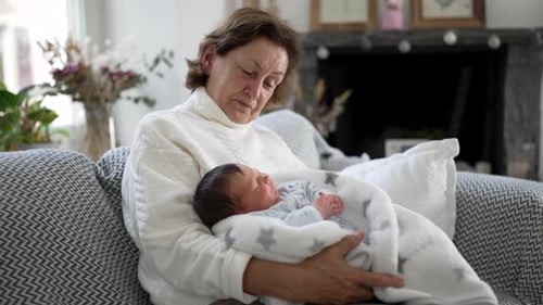 Senior Woman Holding Newborn Baby on Couch Indoors