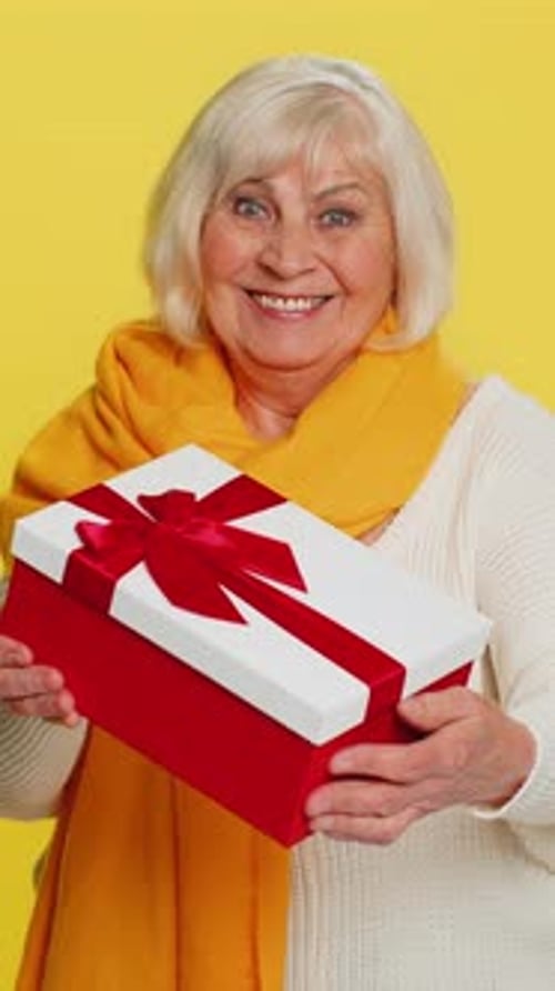 Smiling senior woman holding gift against yellow backdrop