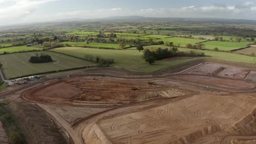 Revealing drone shot of a sand quarry, with diggers and bulldozer, surrounded by the British country