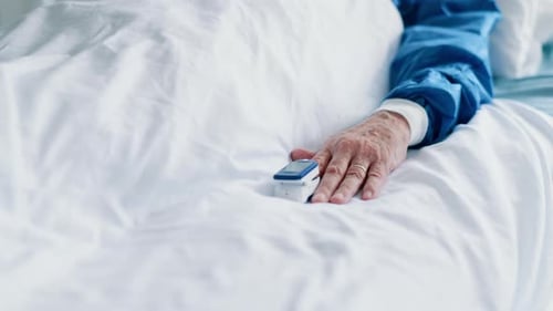 Elderly Patient's Hand Wearing Pulse Oximeter in Hospital Bed