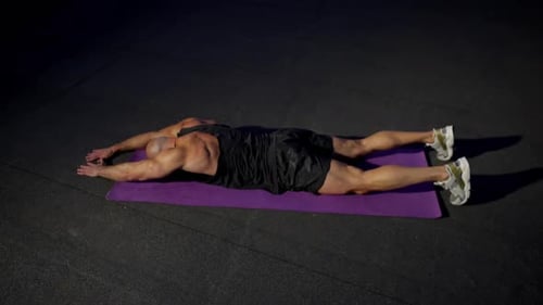 A Man Lying on a Mat Performs a Back Exercise in the Light