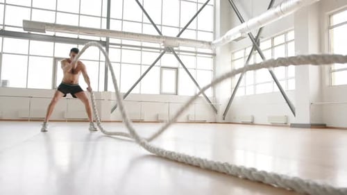 Muscular Man Exercising with Battle Ropes in Gym