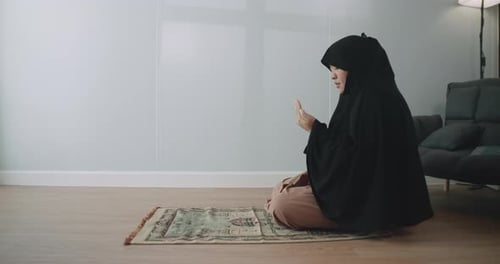 Eine asiatische muslimische Frau im schwarzen Hijab betet mit erhobenen Händen als Segen für Gott.