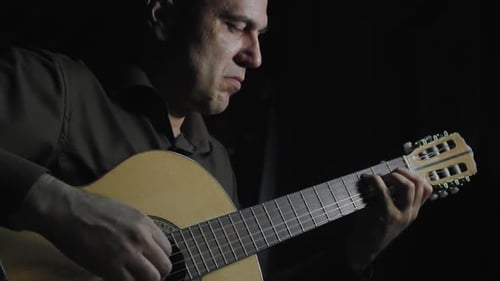 Man Playing Classical Guitar in Dark Setting