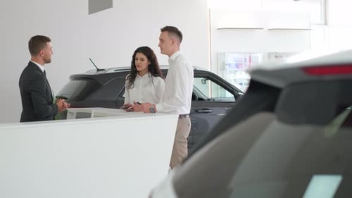 a Man and a Woman are Talking to a Car Dealer in a Car Showroom