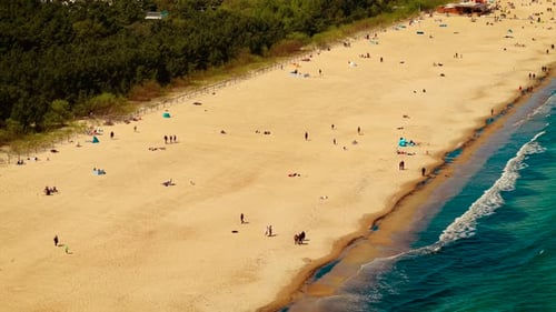 Breiter Sandstrand mit sanften Meereswellen, Menschen entlang der Küste verstreut und genießen die klare Sonne
