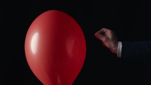 Hand Popping Red Balloon with Pin Closeup on Black Background Happy Birthday