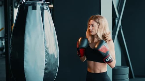 Woman Training With Punching Bag in Modern Gym Setting to Improve Boxing Skills