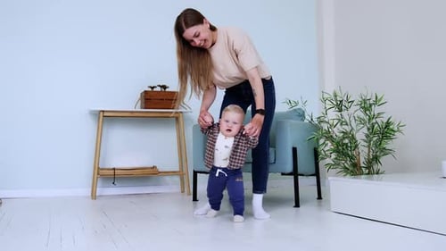 Little sweet boy trying to walk with mom. Woman holding son to make a first steps.