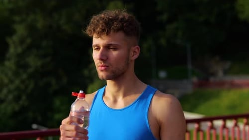 Young Male Runner Drinking Water of Plastic Bottle After Cardio Workout While Standing on the Bridge