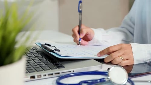 Medical Professional Taking Notes at Computer Desk