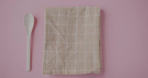 Top View of Hand Putting Half of Juicy Orange on Table Cloth Next to Spoon on Pink Background