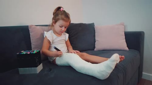Girl Draws on Leg Cast on Couch