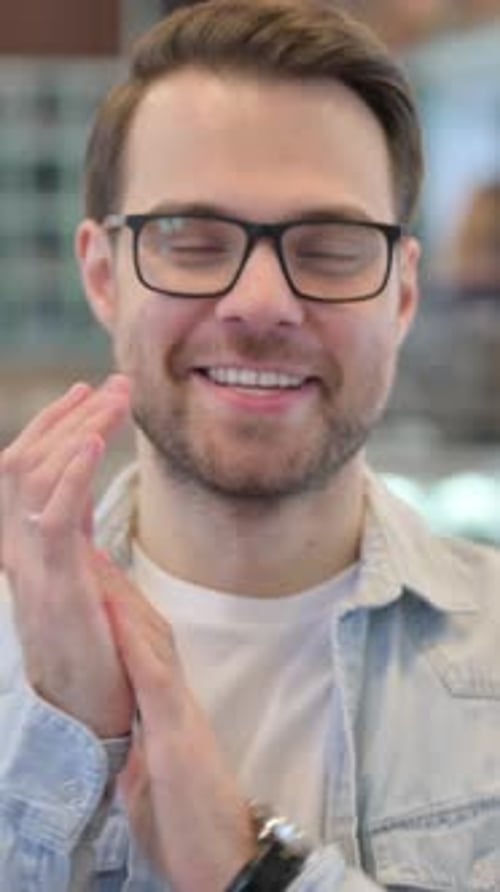 Young Man Smiling and Clapping His Hands Indoors