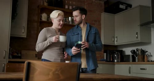 Couple Looking at Phone in Kitchen with Coffee