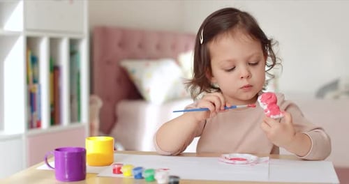 Young Girl Painting a Figurine with Red Paint
