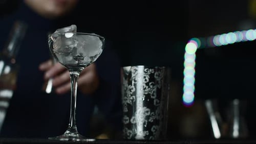Close up of glass with ice cubes prepared for cocktail. Media. Bartender mixing alcohol liquids