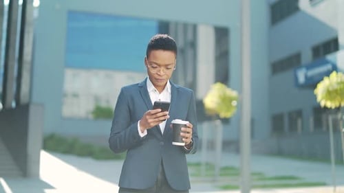successful young confident businesswoman moving with cellphone in hands against modern office