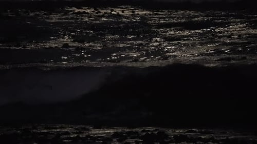Waves crashing onto the shore at night with the moonlight reflecting off the water