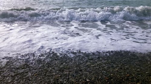 Stormy sea waves splashing onto the pebble beach on a foggy day. Display of nature's power.