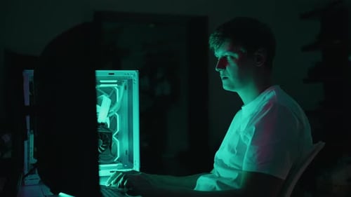 Young Adult Man Types at Computer in Dark Room