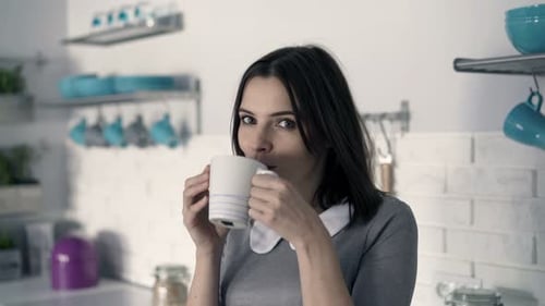 Woman Smiling and Drinking from Mug in Kitchen