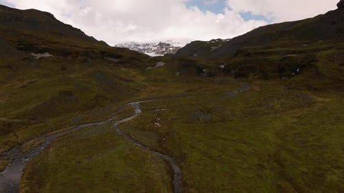 Aerial shot over small glacier rivers revealing snowy mountain top in the distance in Sólheimajökul,