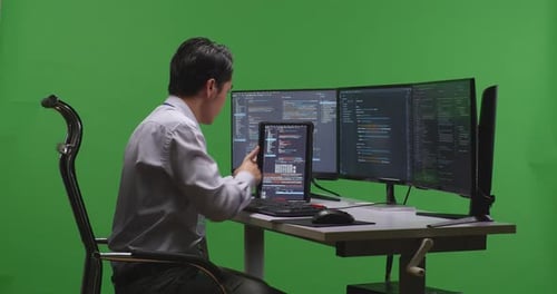 Developer Working With Tablet While Write Code With Multiple Computer Screens In Green Screen Studio