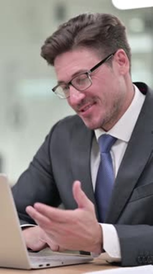 Cheerful Middle Aged Businessman Talking on Video Chat on Laptop in Office, vertical video