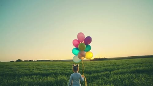 Young Girl With Balloons Standing in Field at Sunrise