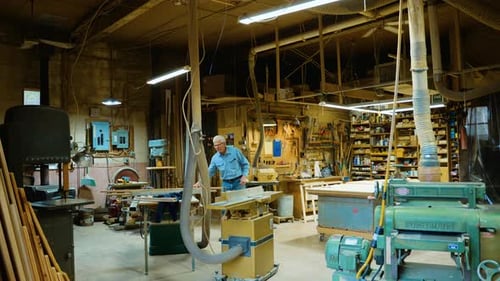 Middle-aged woodworker whittles wood in his workshop, wide shot