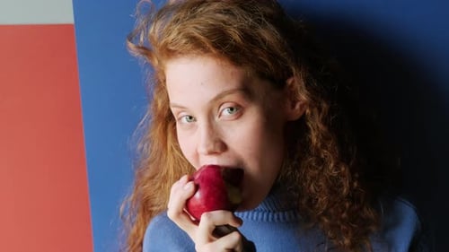 Young Red-Haired Woman Eating Apple at Camera