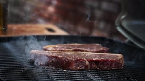 Steaks being cooked on a flaming hot bbq grill and sizzling.